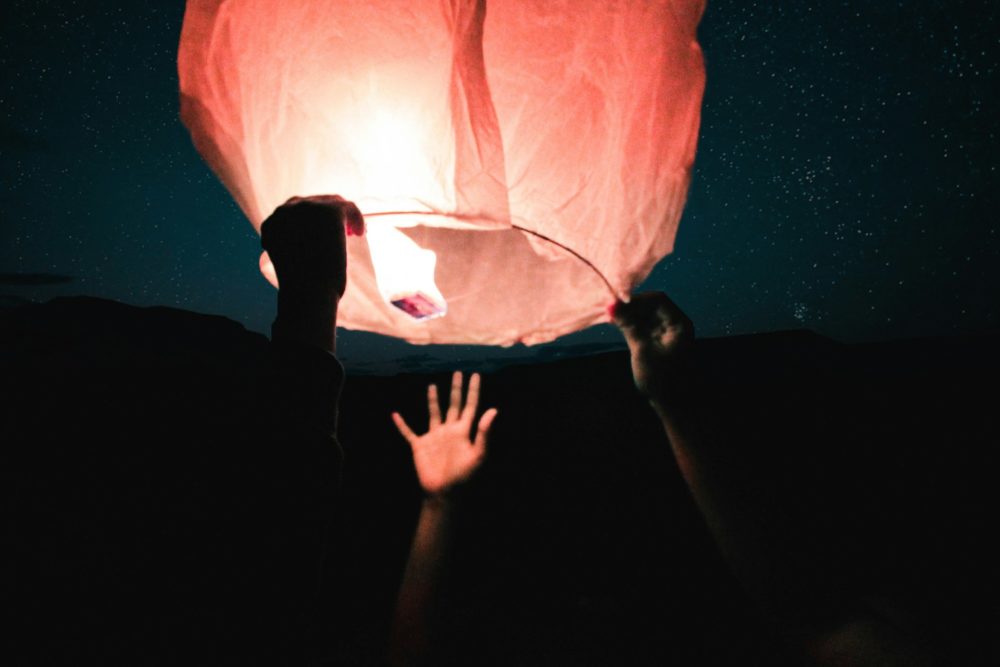 A few hands gather to release a floating candle into the dark night sky